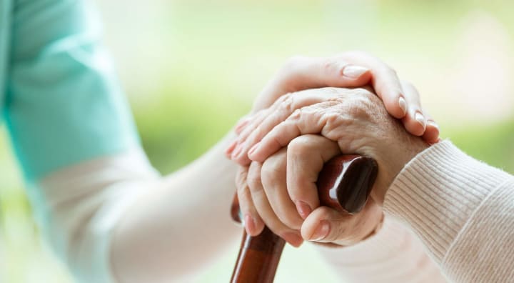 Caregiver holding hands of senior and walking stick