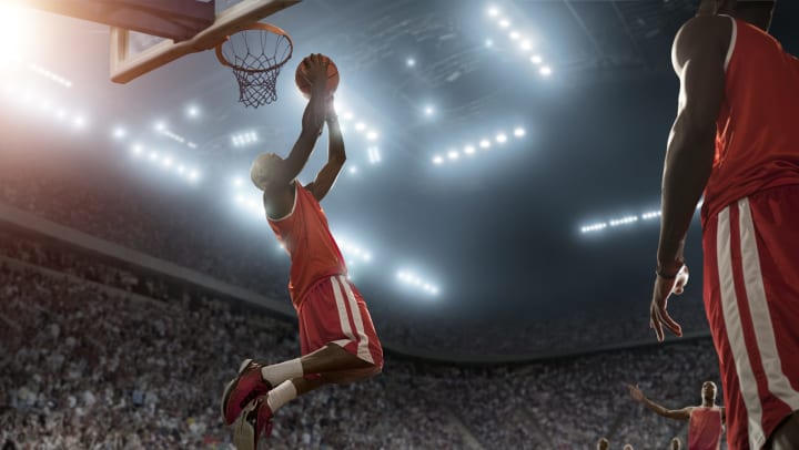 A full basketball player in the background. A man making a dunk in the foreground.