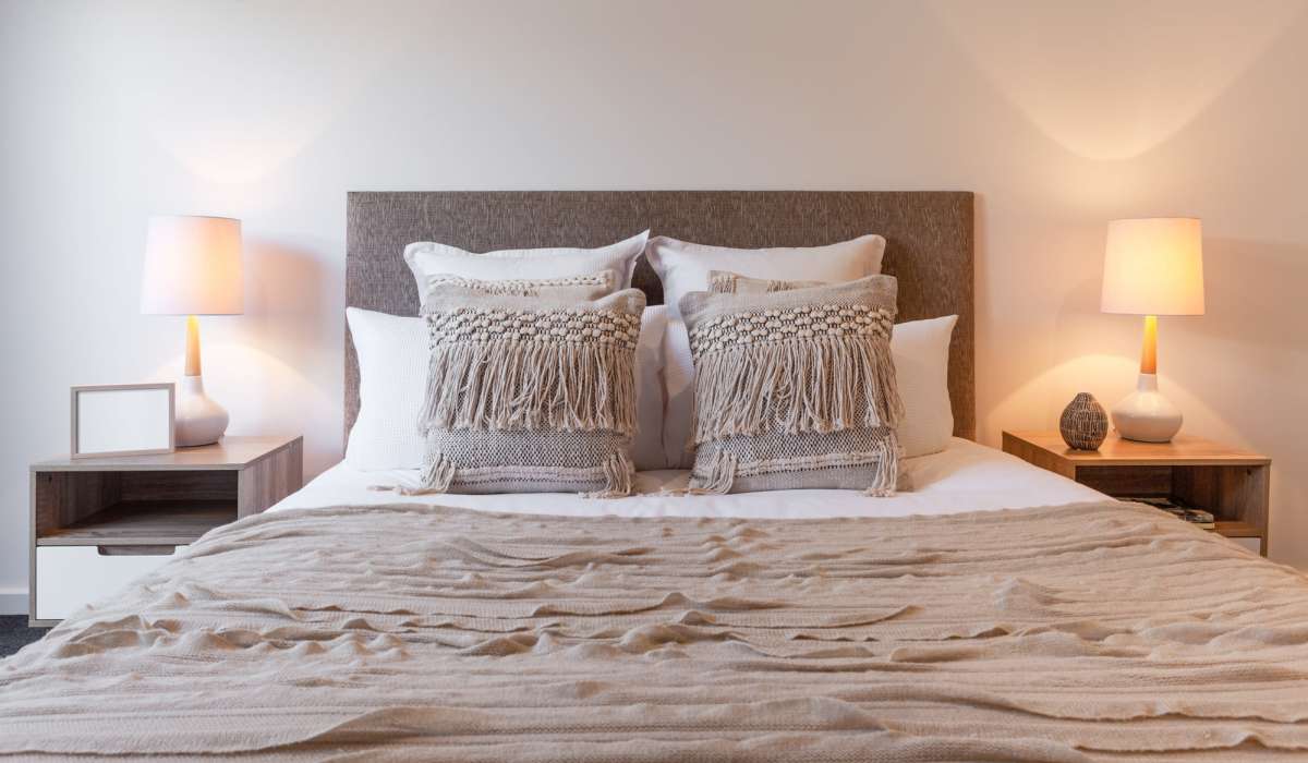 Cozy bedroom with a large bed featuring textured beige pillows and a matching blanket at Dohr Apartments in Rochester, New York