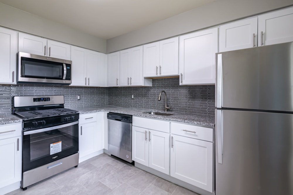 Upgraded kitchen with modern white cabinets, stainless appliances, and granite counters