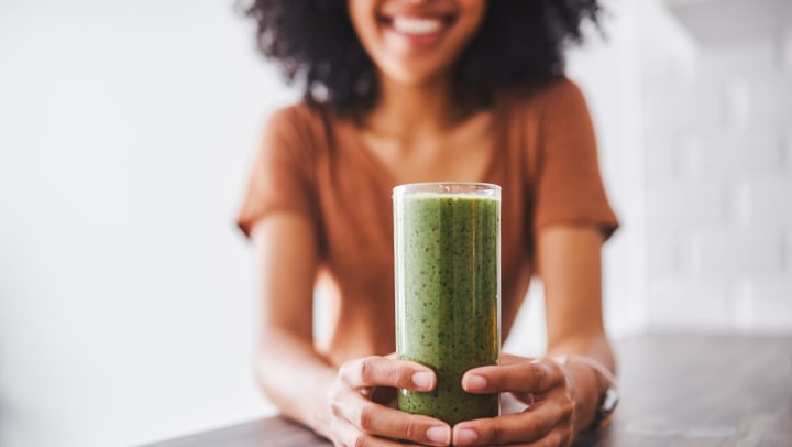 Woman smiling holding a green smoothie on her kitchen counter at Wimberly at Deerwood property