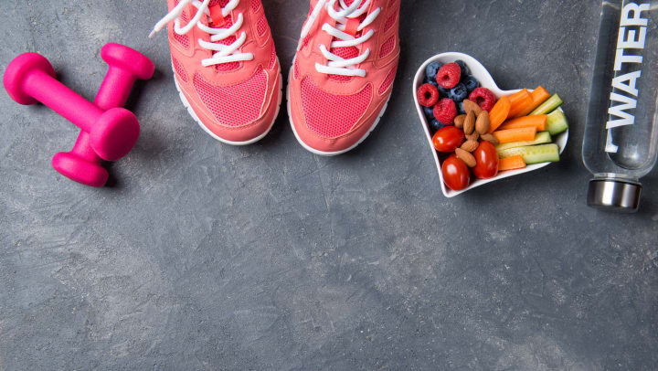 Pink sneakers, dumbbells, bottle of water and a heart-shaped plate with vegetables and berries on a gray background