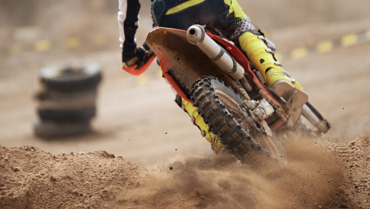 Rear view of a rider on a dirt bike taking a corner during a motocross race.