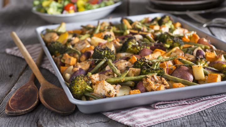 Sheet pan with cooked chicken and a variety of veggies on it. 