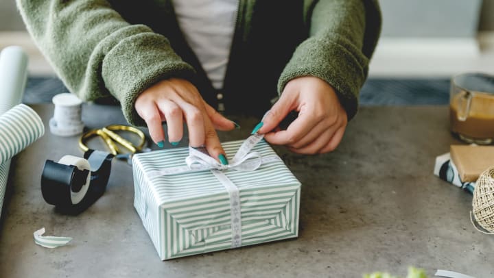 A young woman with teal nail polish tying a bow on a wrapped present