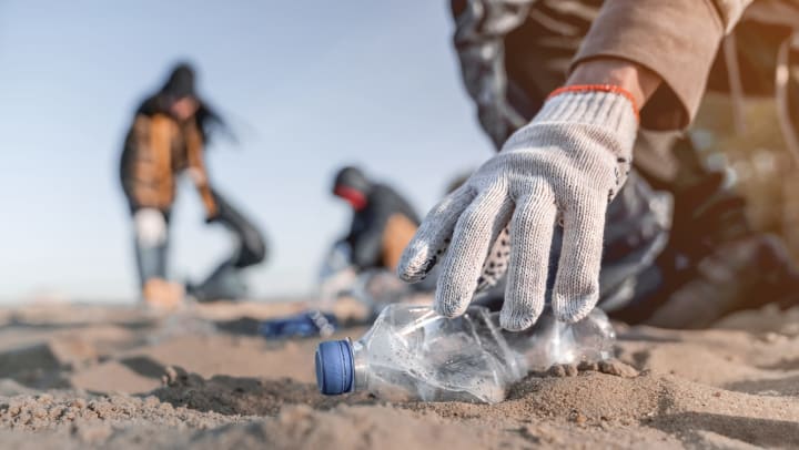 The gloved hand of a volunteer picking up trash on a beach.