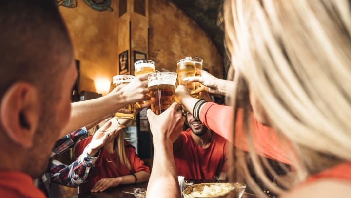 A group of happy friends drinking beer at a brewery all raise their glasses in a toast.