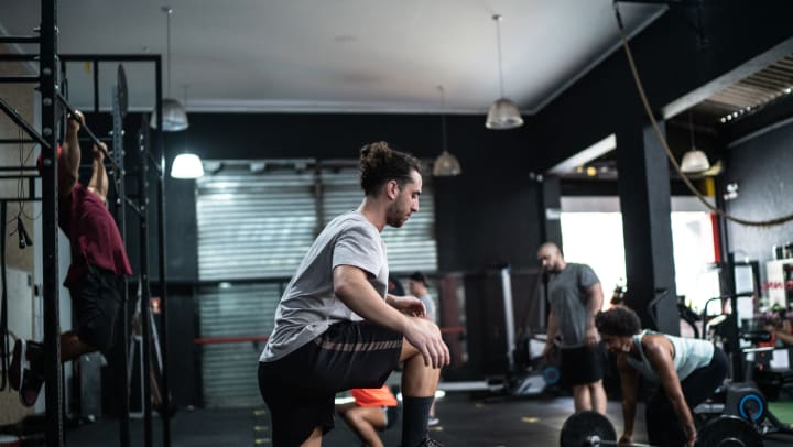Person in CrossFit gym stepping on box, with other people doing various exercises behind.
