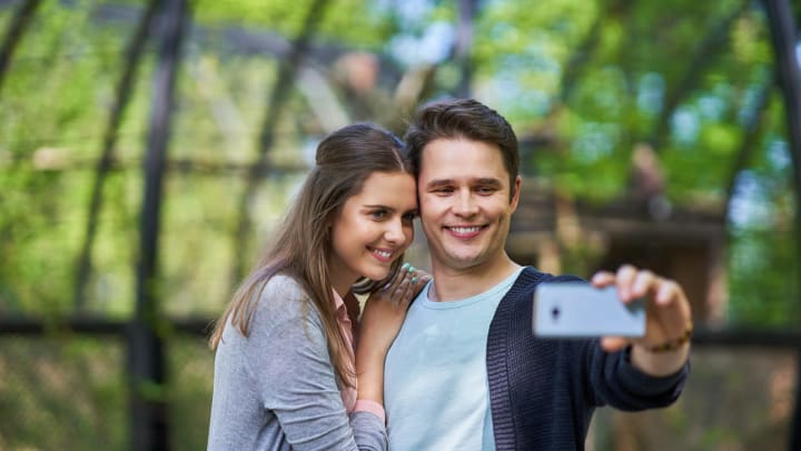 Couple taking a selfie in front of a blurred forest background.