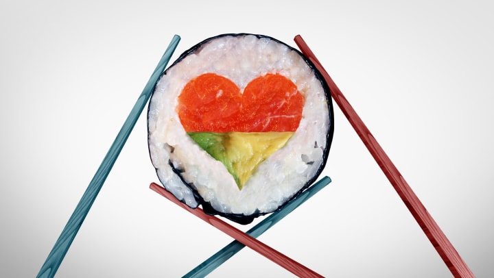 A couple of chopsticks holding a sushi piece with a love heart shape