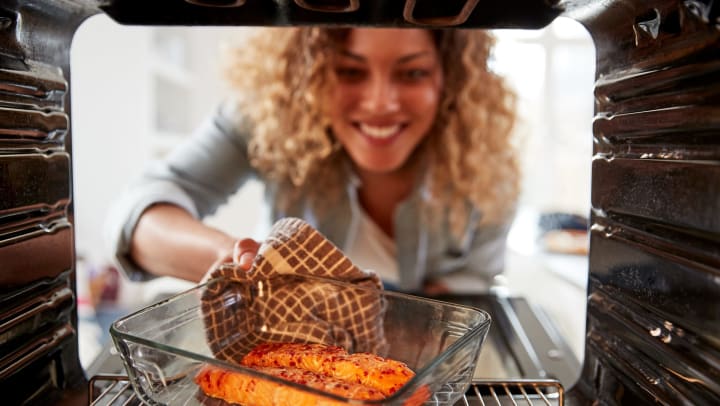 Resident pulling a delicious salmon baked dish out of the oven in her new home at Olympus Grand Crossing in Katy, Texas