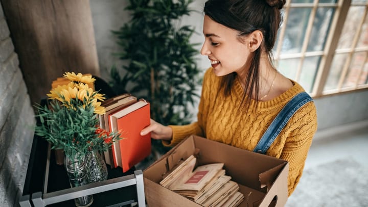 Woman arranging books on a shelf next to a vase of flowers. 