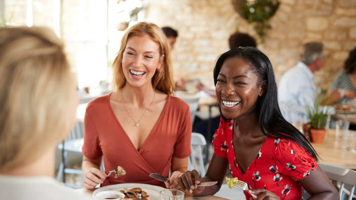Young female friends smiling at brunch in a cafe.