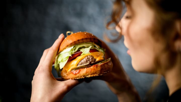 A woman gazes hungrily at a burger she is holding. 