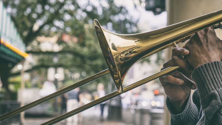 View of a man’s hands holding a shining trombone on a tree-lined street
