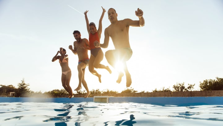 Four happy friends jumping into the swimming pool at the same time.
