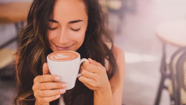 Woman smiling with her eyes closed while holding a latte under her nose.