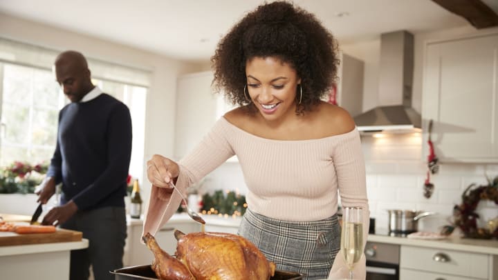 Woman smiling as she bastes a roasting turkey.