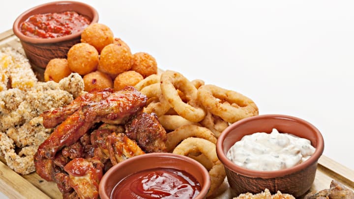 A charcuterie board covered with pub food (buffalo wings, onion rings, etc.) 