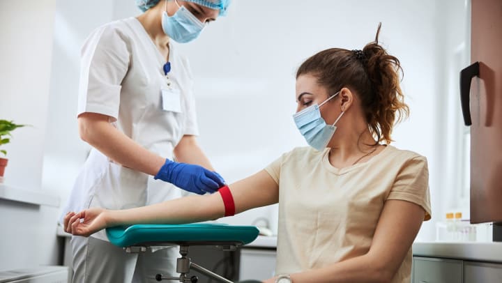 A phlebotomy technician applying a tourniquet to a female patient arm for venipuncture.