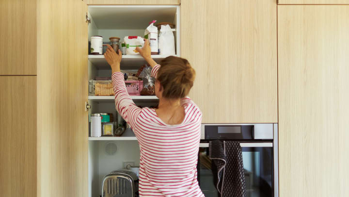A woman in a red striped shirt reaching into an organized kitchen cabinet. 