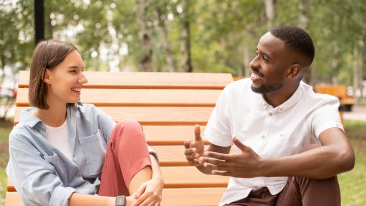 Two people sitting on a bench smiling and talking