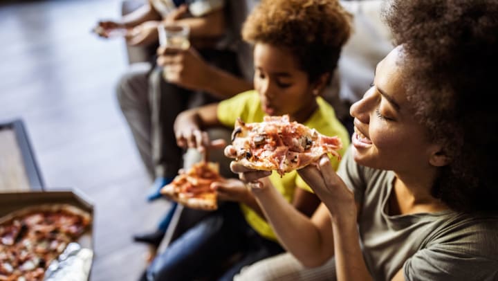A woman and her family eating pizza at home. 