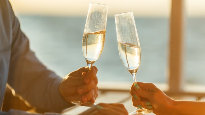 Close-up of couple clinking Champagne glasses over an outdoor table with ocean in background 