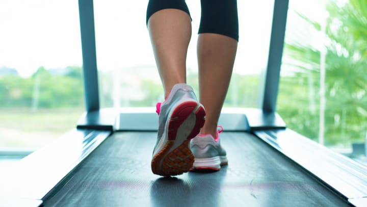 Close up of a woman’s legs in pink and gray sneakers on a treadmill in the gym.