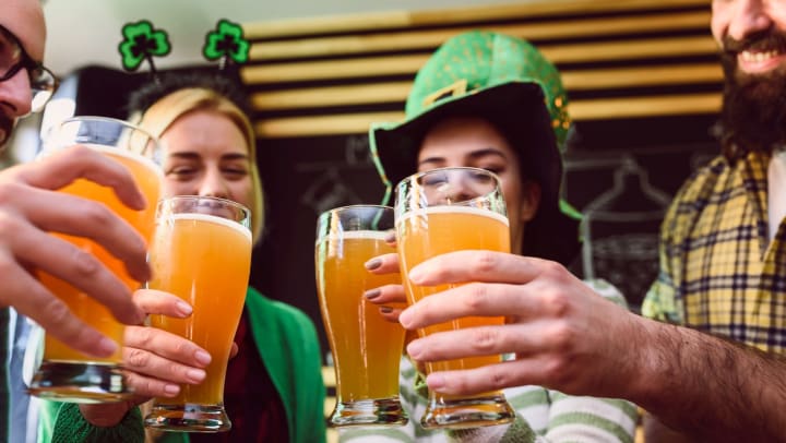 A group of people dressed in green shamrock hats raise their glasses of beer.