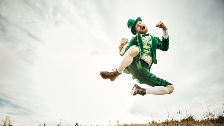 A person dressed as a leprechaun leaps in the air.