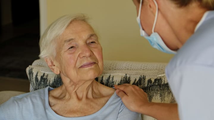 Older woman sitting in her living room being comforted by a nurse