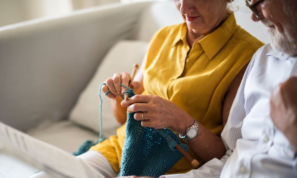 Two residents sitting on a couch, one of them knitting at Randall Residence at Encore Village in Brighton, Michigan
