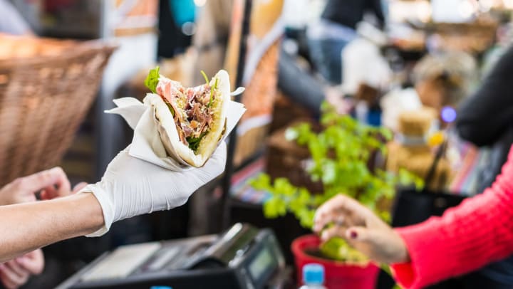 Person handing stuffed tortilla to someone at an outdoor market