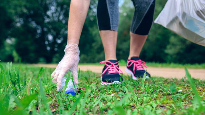 Close up shot of a woman’s hand picking up a water bottle off the grass while doing a volunteer clean-up.