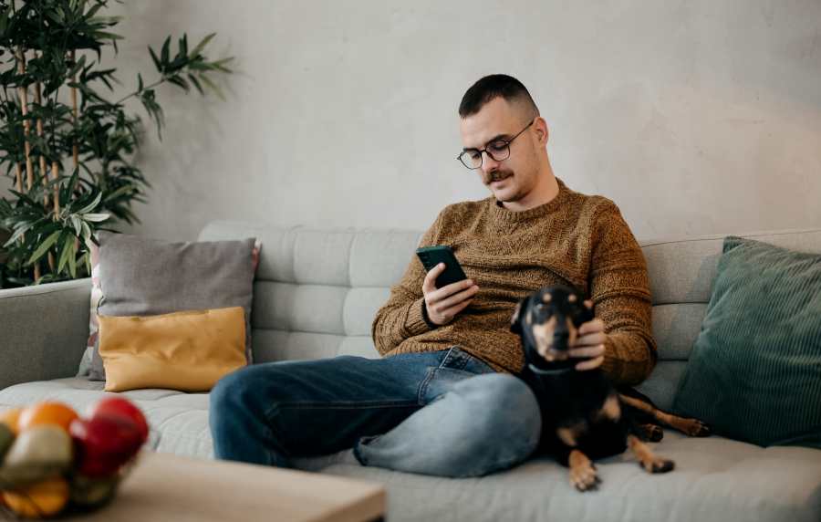 Resident sitting on a couch with his pet dog and checking on his phone in the hand at Charleston Square Apartments in Columbus, Indiana
