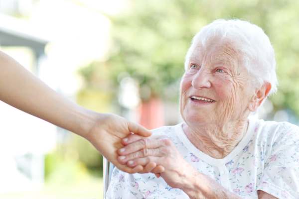 resident in a chair reaching for an outstretched hand at O'Fallon in O'Fallon, MO