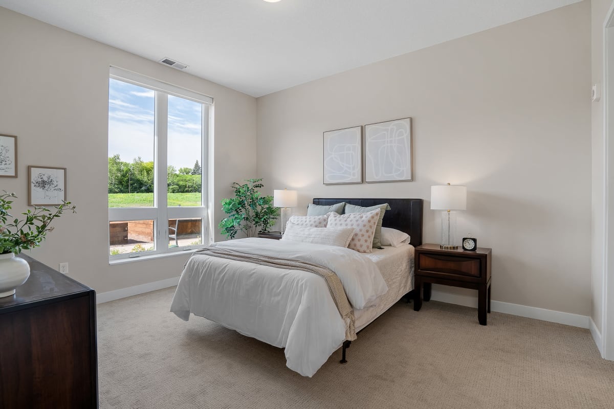 Bedroom furnished with a bed, nightstands, and a dresser in a model senior apartment at Amira Minnetonka in Minnetonka, Minnesota