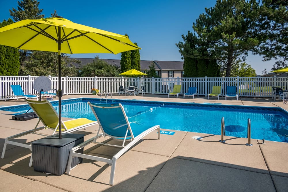 Lounge chairs with shade umbrella by pool at Waters Edge Apartments in Lansing, Michigan