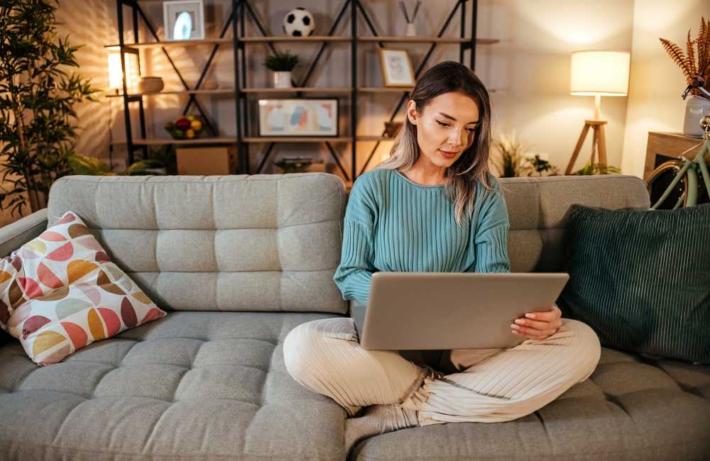 A resident sitting on the couch and working on her laptop in a modern living room at Parc at Prairie Grass Apartments in Colorado Springs, Colorado