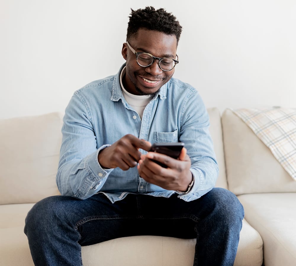 A man smiling at his phone while sitting on his couch at Windsor Park in Woodbridge, Virginia