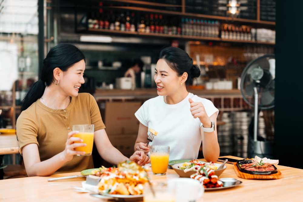 Two women enjoying a meal together, smiling and sharing drinks at a restaurant table at Mapleton Properties in Indianapolis, Indiana