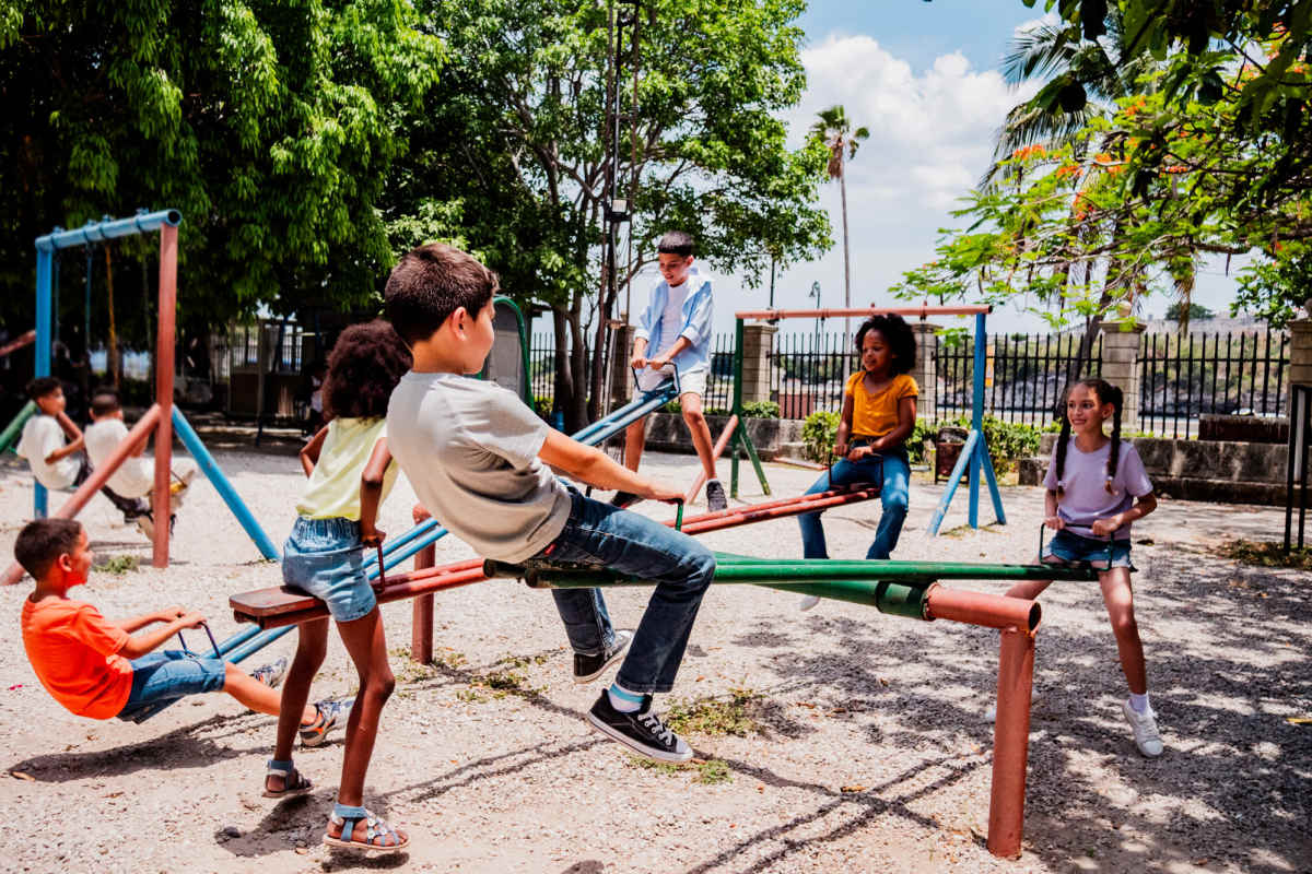 Children playing on seesaws and swings in a vibrant playground surrounded by trees at Sunflower Estates in Indianola, Mississippi