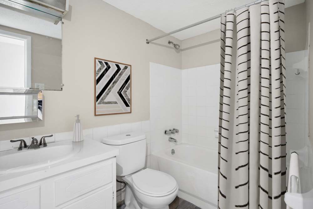 Clean bathroom with bathtub, shower curtain, and modern vanity at Granada Gardens Apartments in Warrensville Heights, Ohio