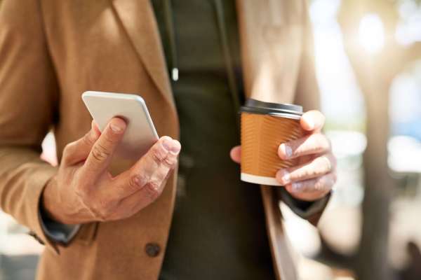 A man holding his phone and coffee at Raystone Apartments in Phoenix, Arizona