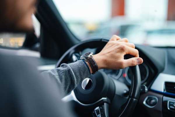 Man driving with hand on steering wheel, watch visible at Whispering Wind Apartments & Townhomes in Newtown, Ohio