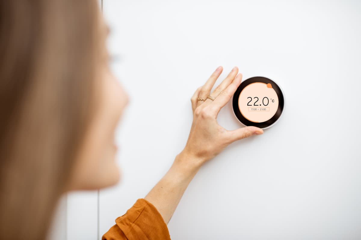 Close up of young woman adjusting central heating temperature at home on thermostat at Traditions at Englewood in Englewood, Colorado