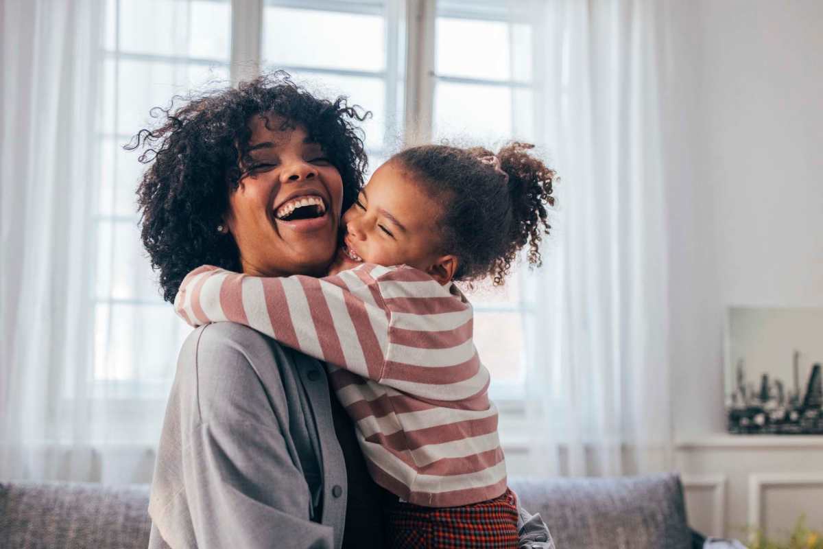 A joyful woman and child embrace in a sunlit room, both smiling broadly at Naranja Villas in Naranja, Florida
