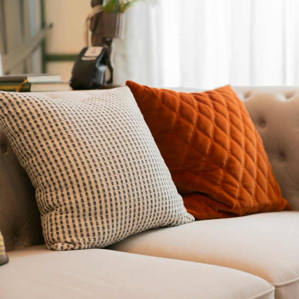 Tufted beige sofa with textured white and rust-colored accent throw pillows at Ember Ridge Apartments in Pensacola, Florida