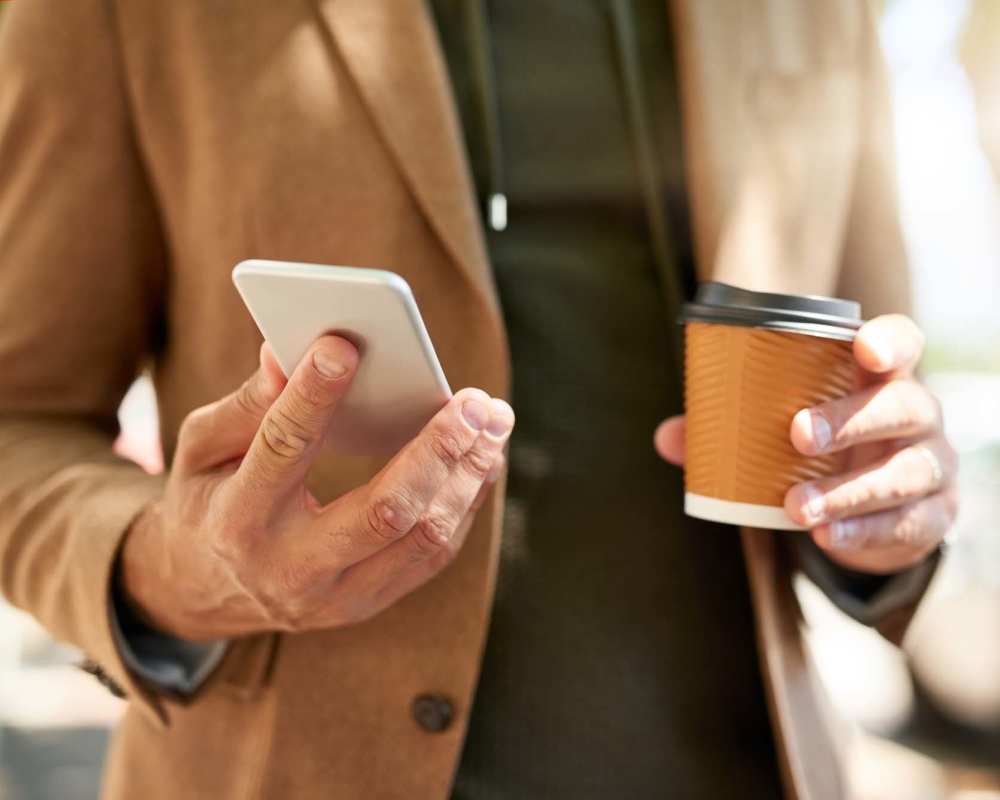 Resident checking his phone while holding coffee in other hand at The Crossings At Valley View in Bloomington, Minnesota 